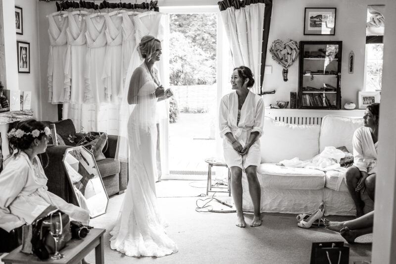 www.bridebook.co.uk bride in her dress as bridesmaid looks on smiling 
