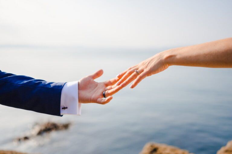 Bride's hand with engagement ring reaching out to touch groom's hand with wedding ring