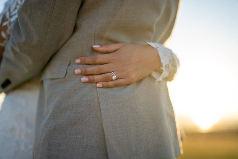 Bride's hand with diamond engagement ring wrapped around groom in loving embrace