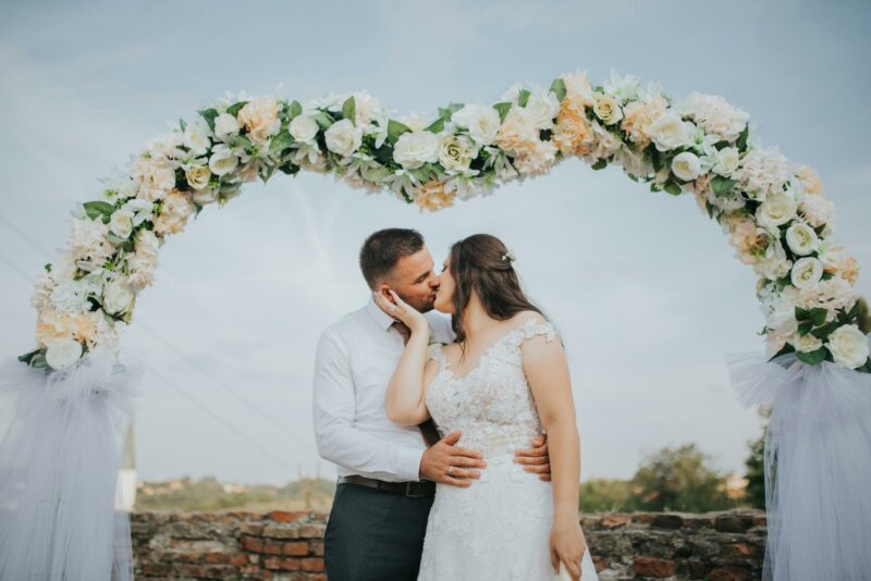 Married couple kissing below a flower arch