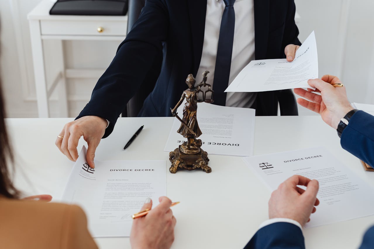 Réunion juridique autour d’un divorce, avec un avocat distribuant des documents intitulés "Divorce Decree" et une statue de Lady Justice sur la table.