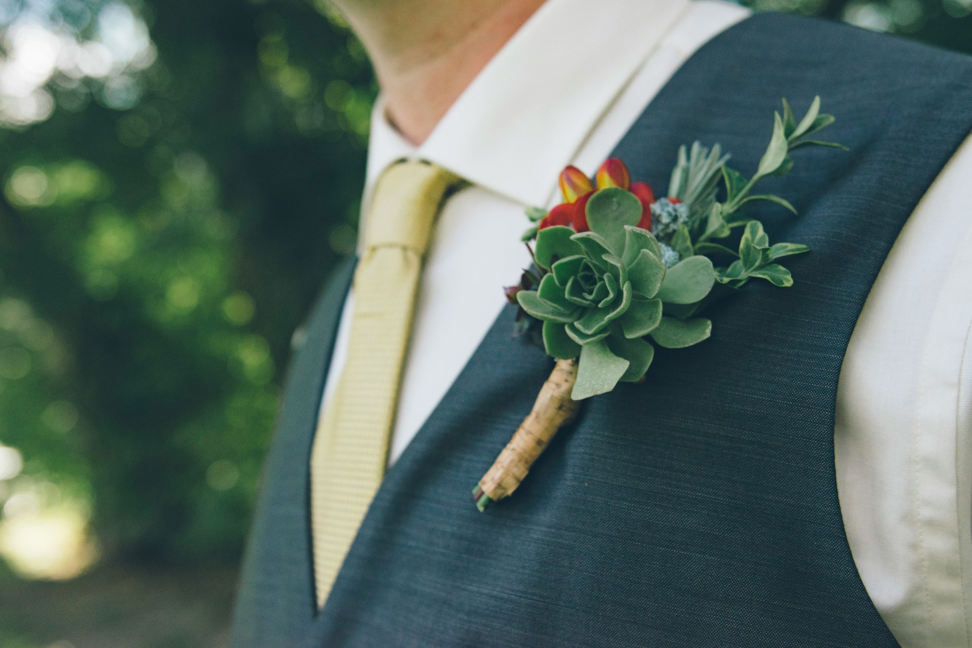 Gros plan sur une boutonnière florale épinglée sur un costume, mettant en valeur un détail subtil mais essentiel du look du marié.