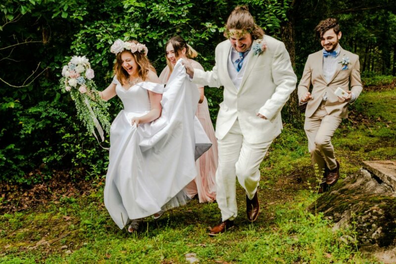 Couple de mariés et leurs invités en train de courir dans l'herbe