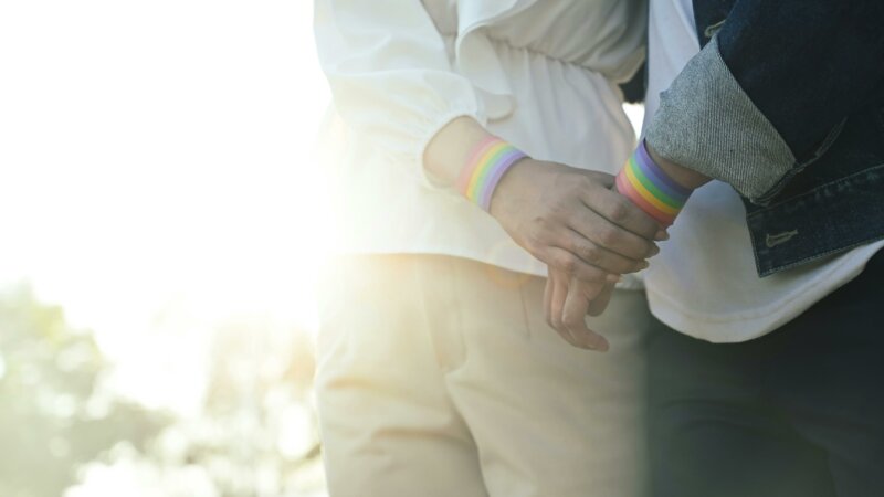 Couple se tenant la main avec bracelets aux couleurs du drapeau LGBT